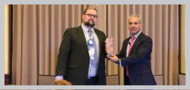 a photo of Mr Simon Spencer, NBA's CIO, receiving the award from Mr Mohit Sagar, Editor in Chief and MD of Open Gov