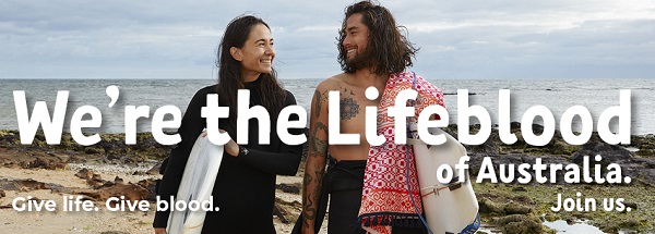 Image of two surfers (woman and man) in wetsuits emerging from the ocean with surfboards smiling. 